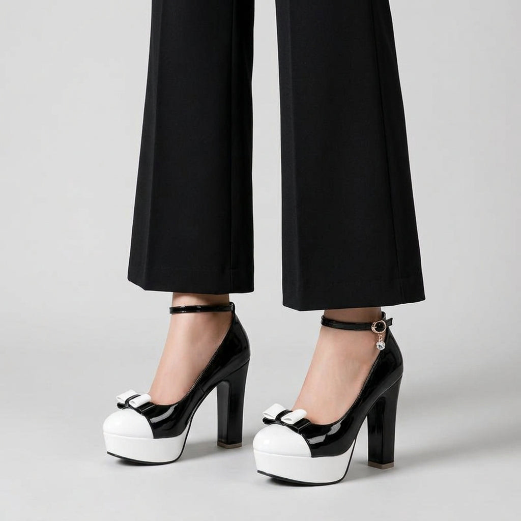 Black and white platform high heels with ankle straps and bow details, shown on a model wearing black leather pants in a bright, modern room.