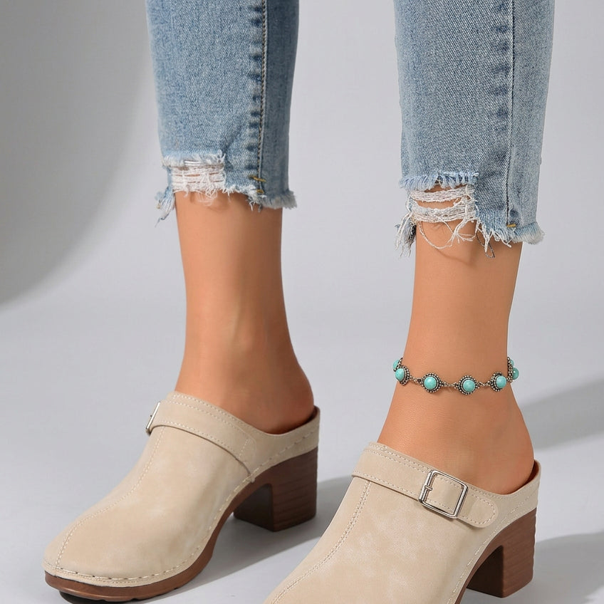 Beige clogs with brown soles worn on a beach setting