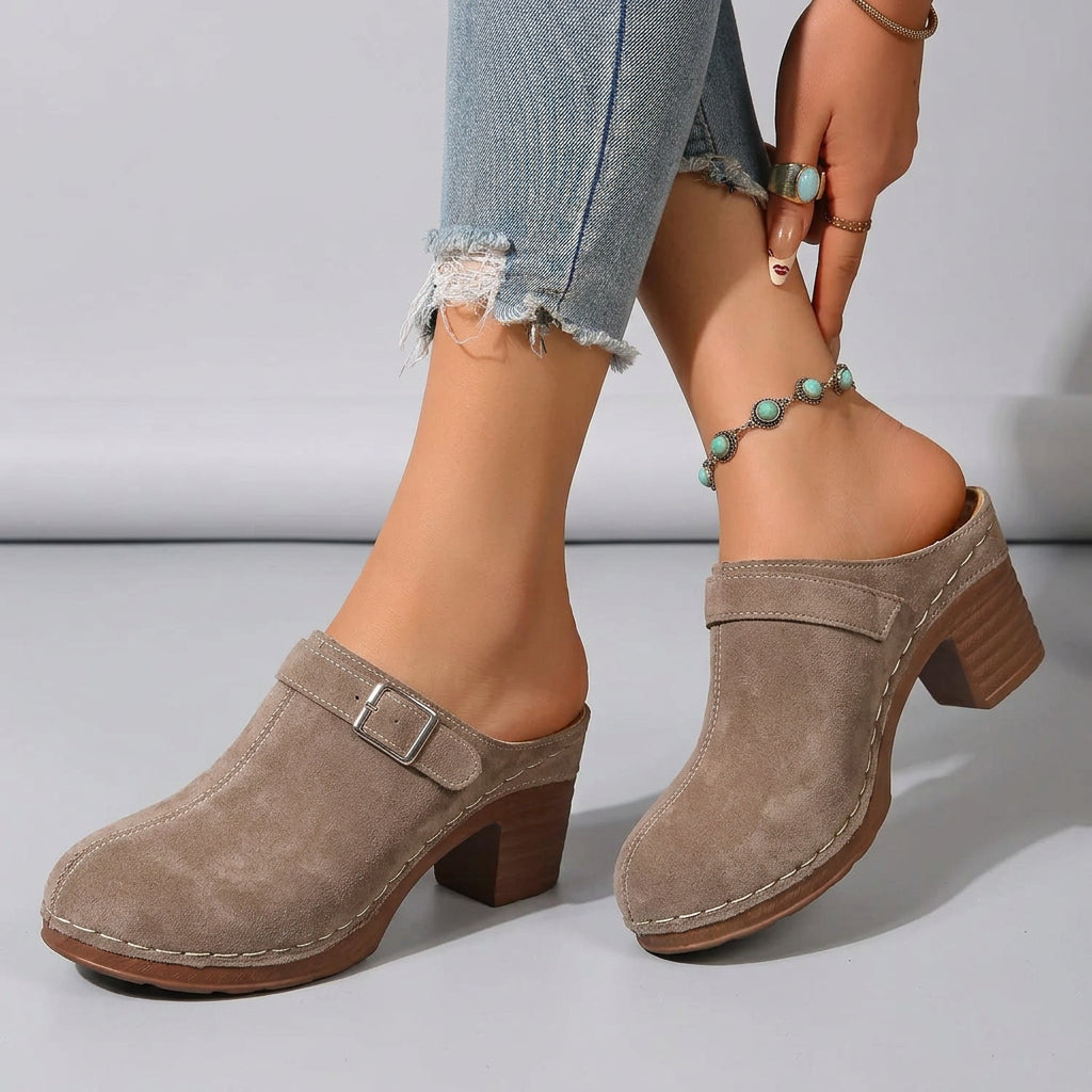 Brown clogs worn by a person on a mosaic floor with a sandy background