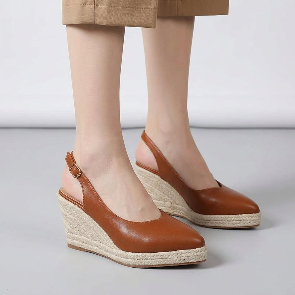 Brown wedge sandals with espadrille sole worn by a person on a light gray floor.