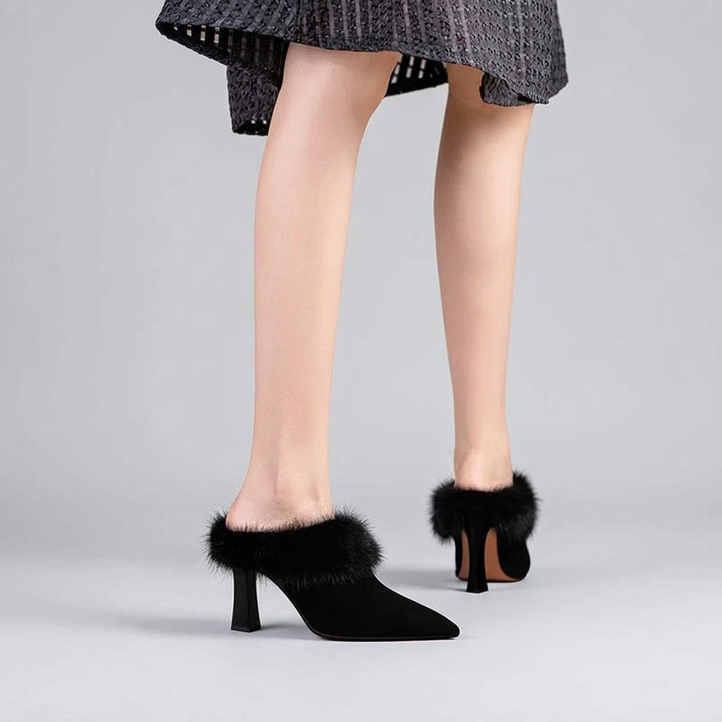 Black high-heeled shoes with fur trim worn by a person on a beige background